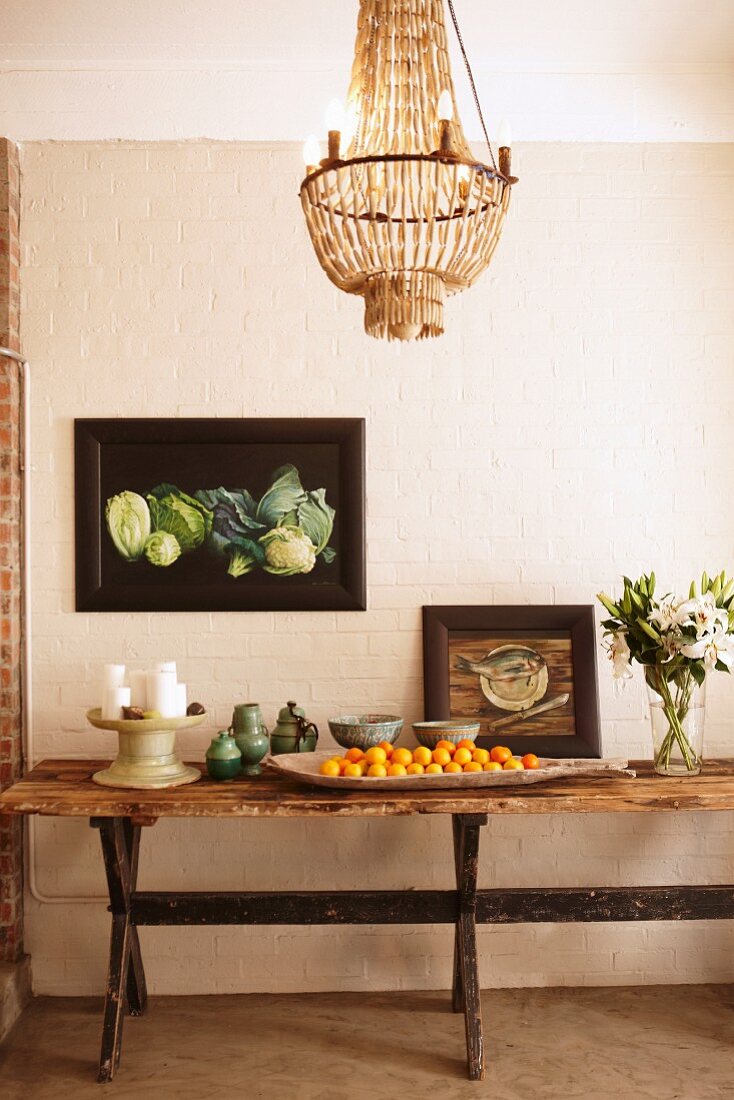Rustikaler Holztisch dekoriert mit Keramik- und Porzellangeschirr, Blumenstrauß und Obstschale, Vintageflair mit gerahmten Gemälden und Kronleuchter