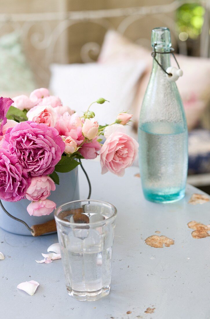 Emailletopf mit verschiedenfarbigen Rosen zwischen Trinkglas und Vintage Flasche mit Schnappverschluss