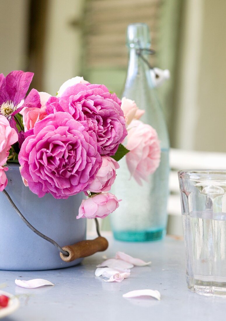 Rosenstrauss in Emailletopf und Trinkglas auf Tisch
