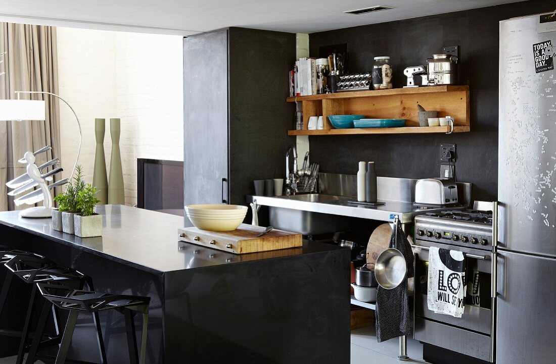 Black island unit opposite workbench-style kitchen counter and wooden shelves on dark wall