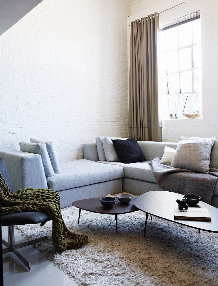 Pale grey corner sofa and set of coffee tables on flokati-style rug in corner