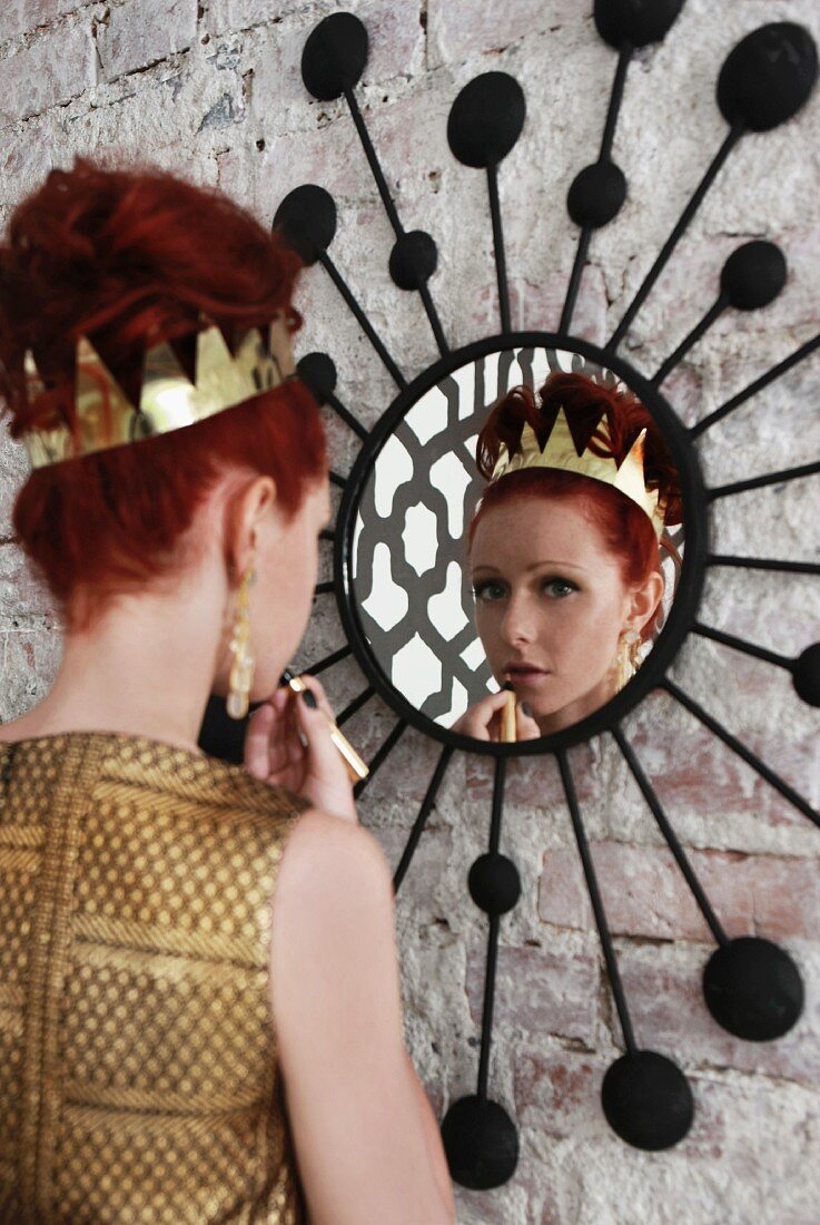Festively dressed woman with crown in hair applying makeup in front of mirror