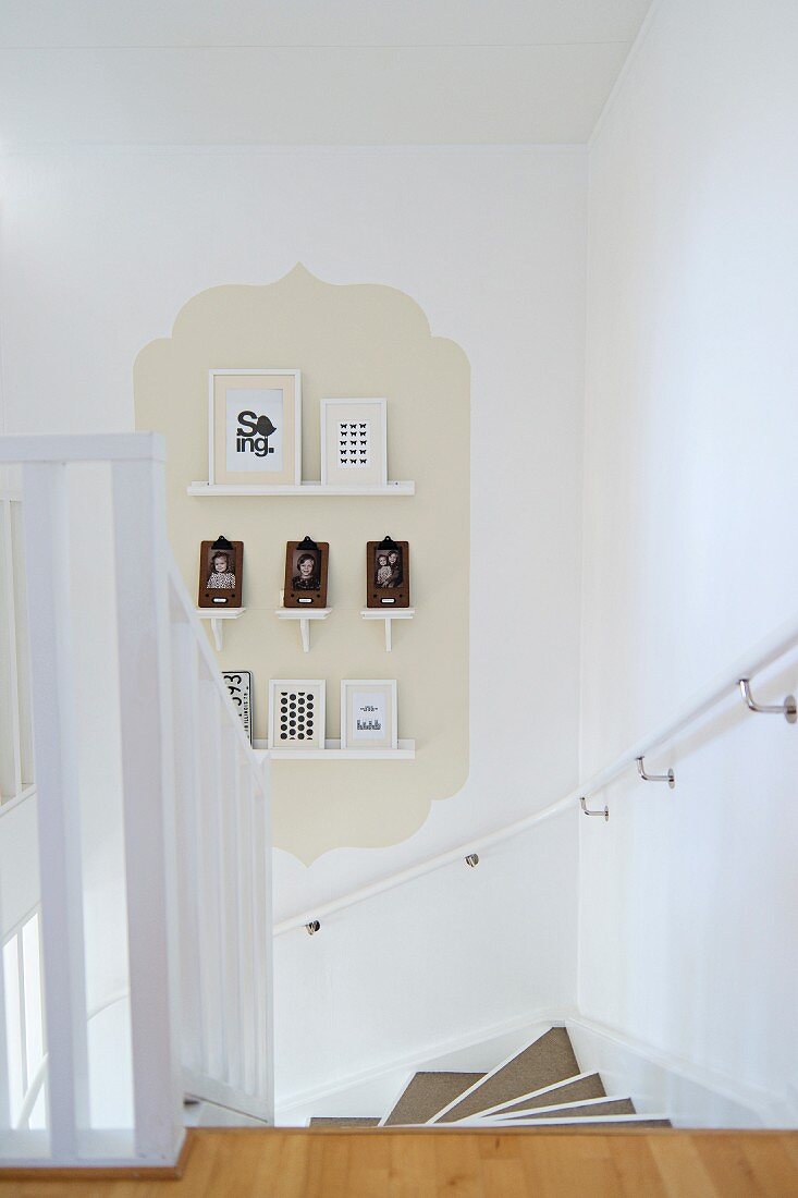 Blick von Treppenabgang auf kleine Galerie gerahmter Bilder vor beige getöntem Hintergrund in Form eines klassischen Fliesenmotivs