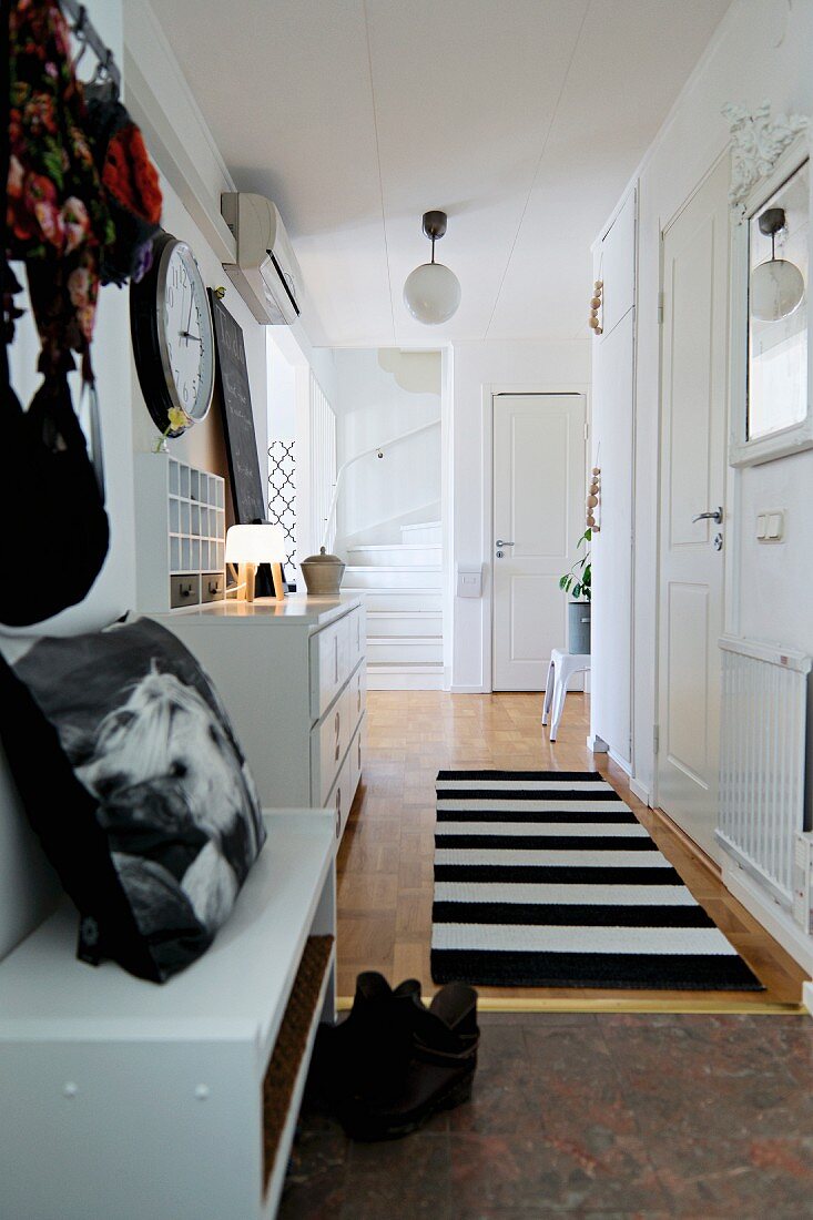 White hallway with black accessories, runner with wide stripes and foot of staircase at far end