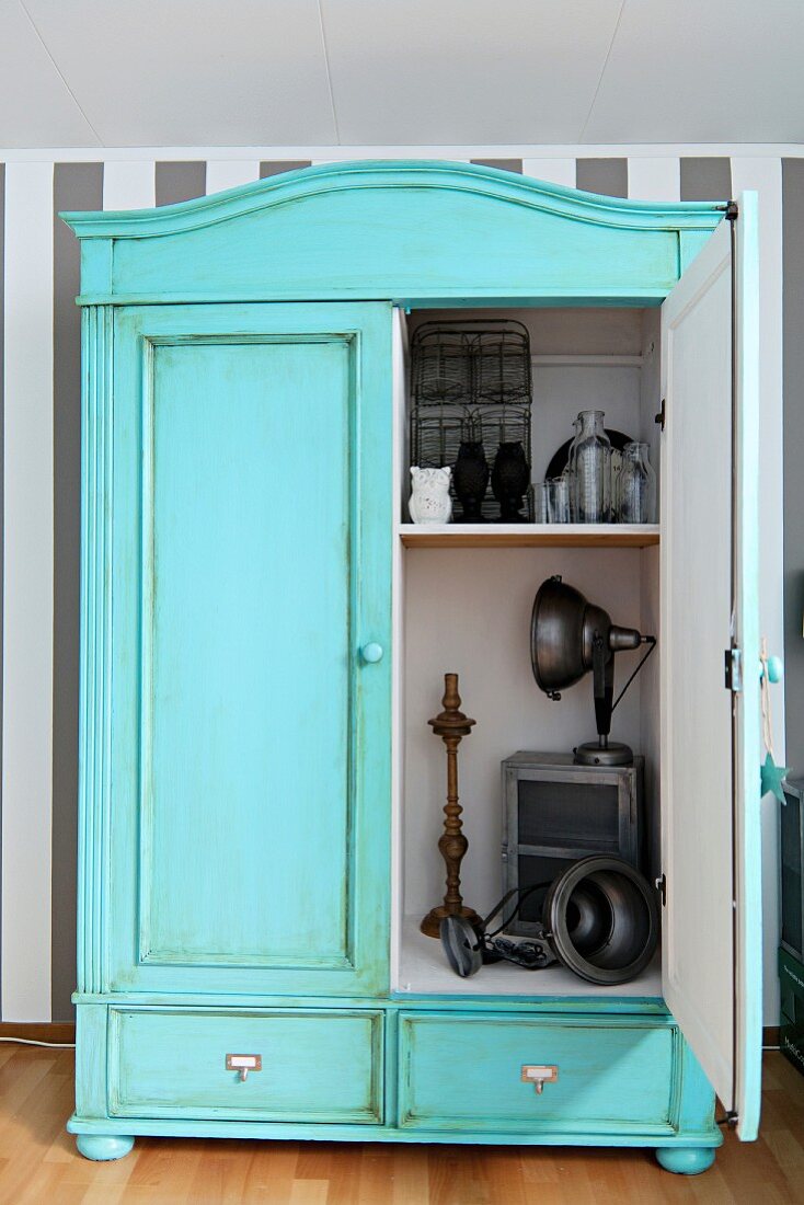 Pastelltürkis gestrichener Vintage Schrank mit Patina, Blick durch die offene Tür auf Deko Objekte