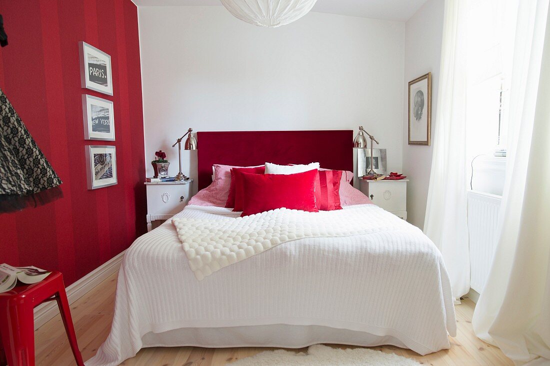 Gerahmte Bilder an rot gestreifter Wand, daneben ein Bett mit rotem Kopfteil im Schlafzimmer