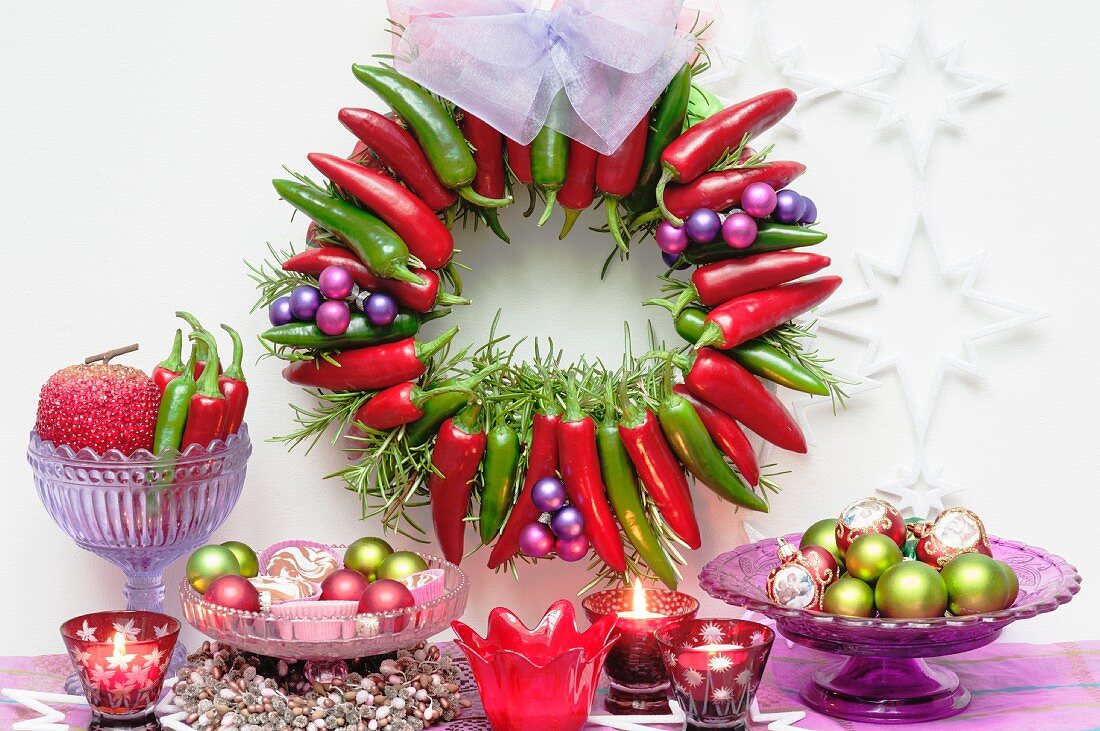 Adventskranz an der Wand aus roten und grünen Chilischoten, Kugeln, Kerzen und Sterne als Weihnachtsdeko