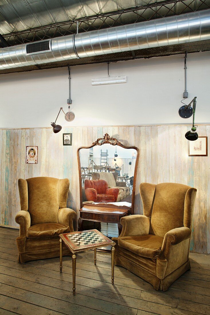 Gemütliche Sitzecke mit Schachbrett-Tisch und plüschigen Lesesesseln vor großem Wandspiegel
