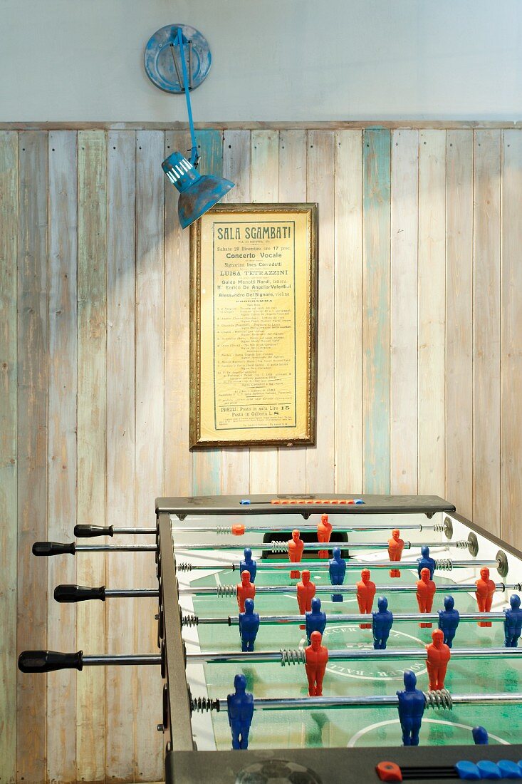 Illuminated games area with football table and simple wood-panelled wall