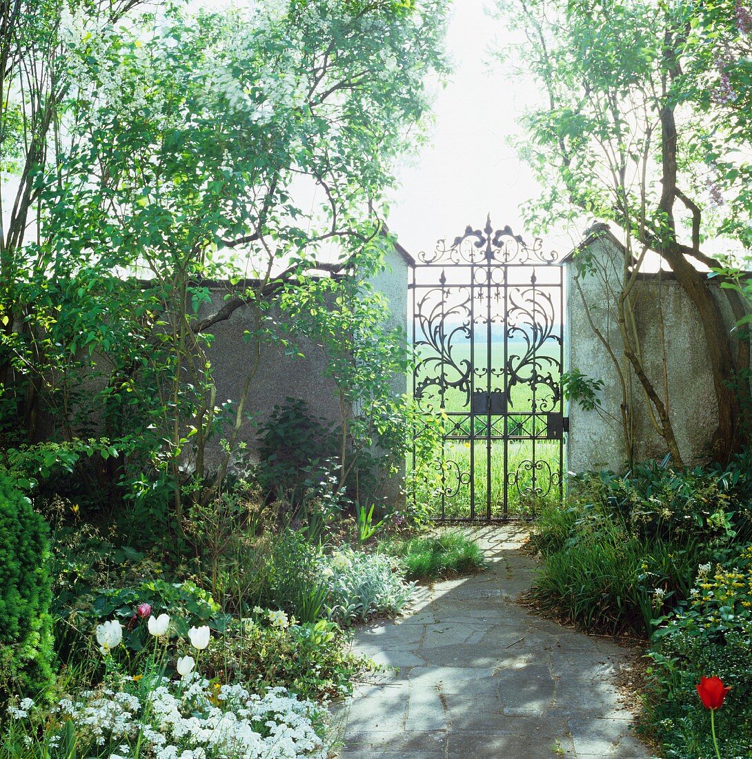 Blick auf frühlingshaften Garten mit Gartenmauer & schmiedeeisernem Tor