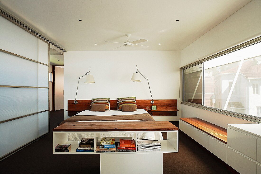 Halbhohes Regal vor Doppelbett mit flankierenden Nachttischleuchten in modernem Schlafzimmer mit Glasschiebeelement