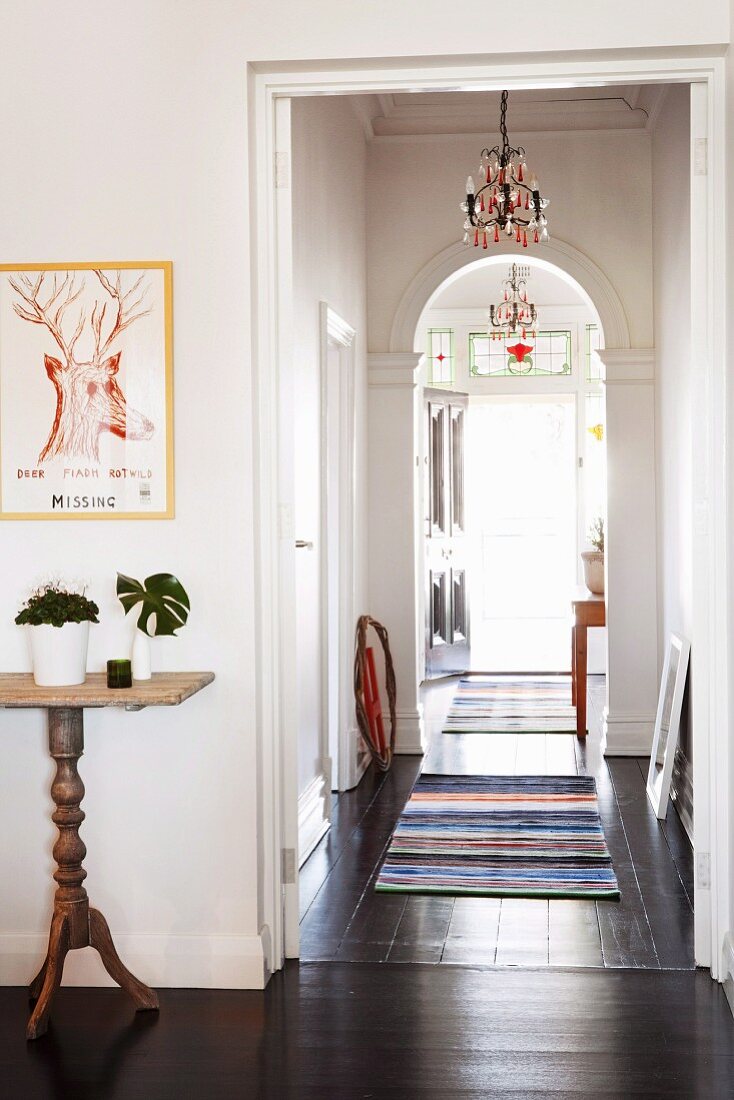 View along narrow hallway with dark wooden floor, arch & striped rugs