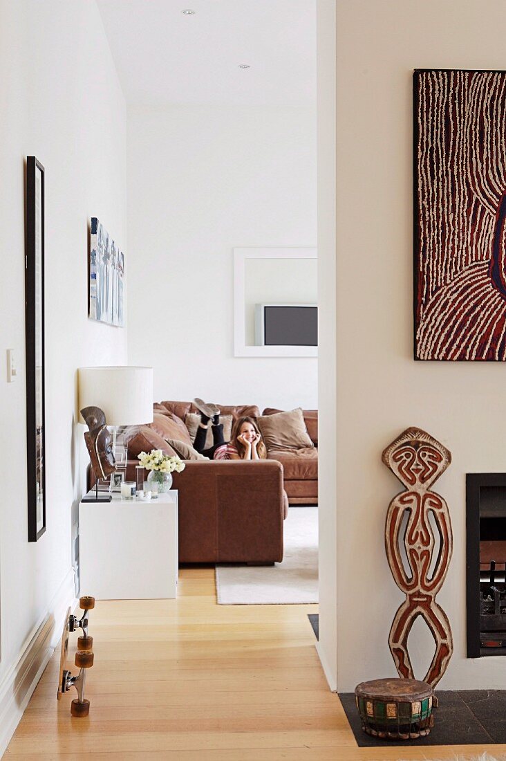 Kunsthandwerkliche Dekoobjekte vor Wand neben raumhohem Durchgang zum Wohnzimmerbereich mit Couchgarnitur