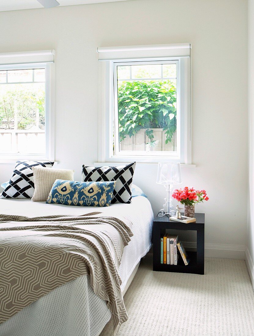 View though open door of modern bed with scatter cushions and cubic side table below window