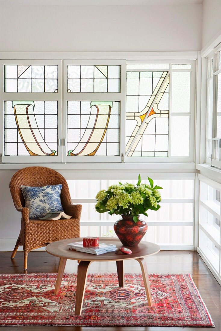 Blumenvase auf niedrigem Beistelltisch im 50er Jahre Stil und Rattanstuhl vor Fenster mit Verglasung im Jugendstil