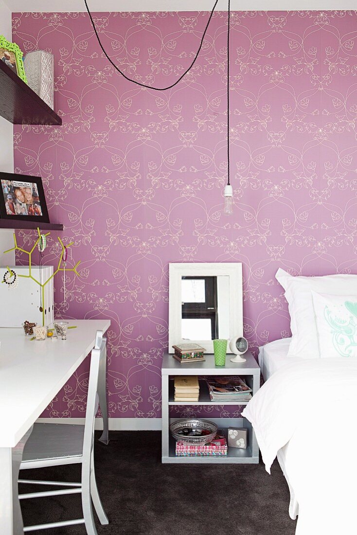 Bedroom with bed, bedside table & desk in front of wall with purple patterned wallpaper