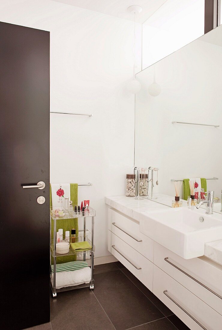 View into modern bathroom with white washstand, base units & mirrored wall