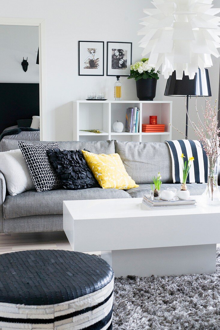 Weisser Couchtisch vor grauem Sofa mit bunten Kissen in modernem Wohnzimmer