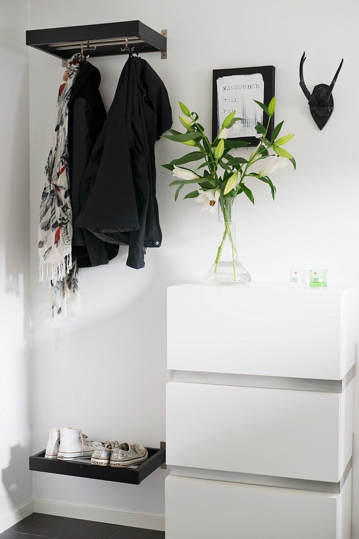 Open-plan cloakroom - jackets hanging from hooks below shelf next to white chest of drawers