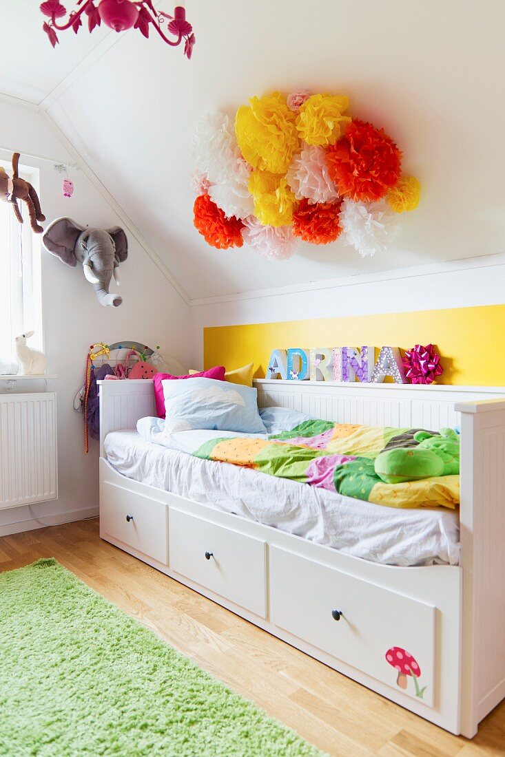 Bett mit weißem Holzrahmen und Schubladen in Kinderzimmer unter dem Dach
