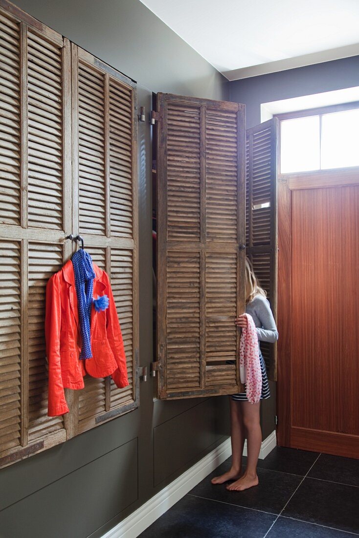 Fitted cupboards with old window shutters as doors, red blazer hanging on coathanger and girl selecting clothes