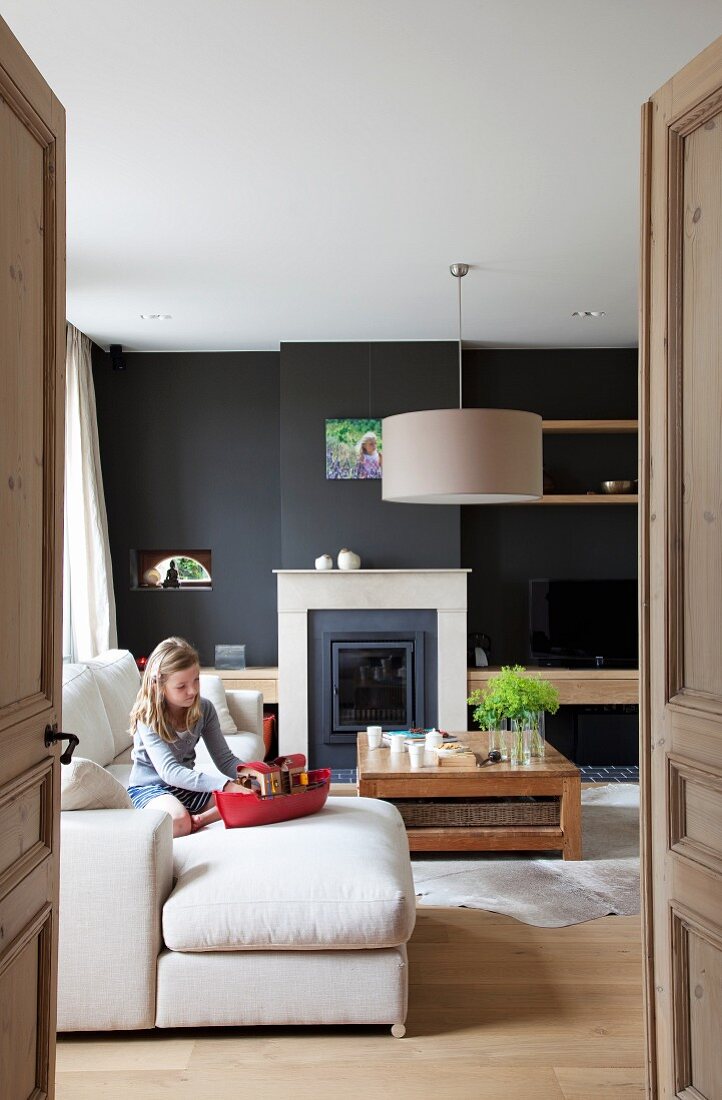 Mädchen mit Spielzeugschiff auf Sofa in modernem Wohnzimmer mit schwarz getönter Wand