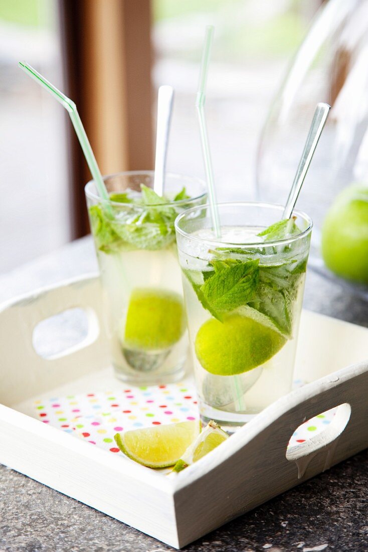 Sommerdrink mit Limette und Minzblättern in Gläsern auf Holztablett