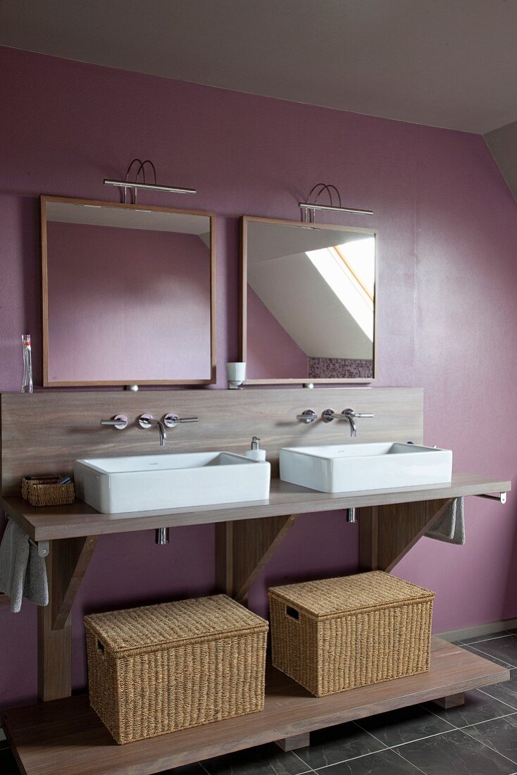 Moderner Doppelwaschtisch mit Aufsatzwaschbecken, Bastkörben und Spiegeln mit Bogenleuchten vor pastellviolett getönter Wand