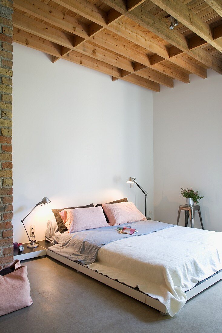 Schlichtes Doppelbett in minimalistischem Schlafzimmer, sichtbare Holzbalkendecke