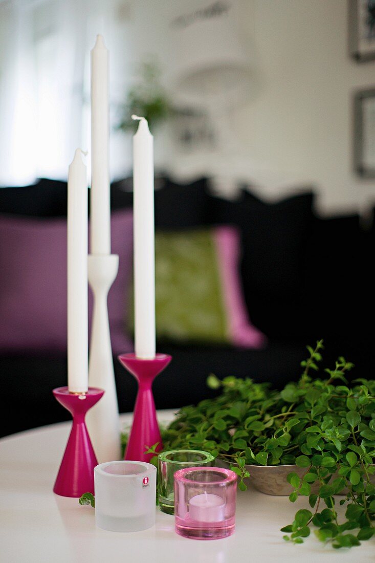 Mehrteiliges Kerzenständer-Set in Pink und Weiß, davor Windlichter, seitlich Schale mit Blätterzweigen