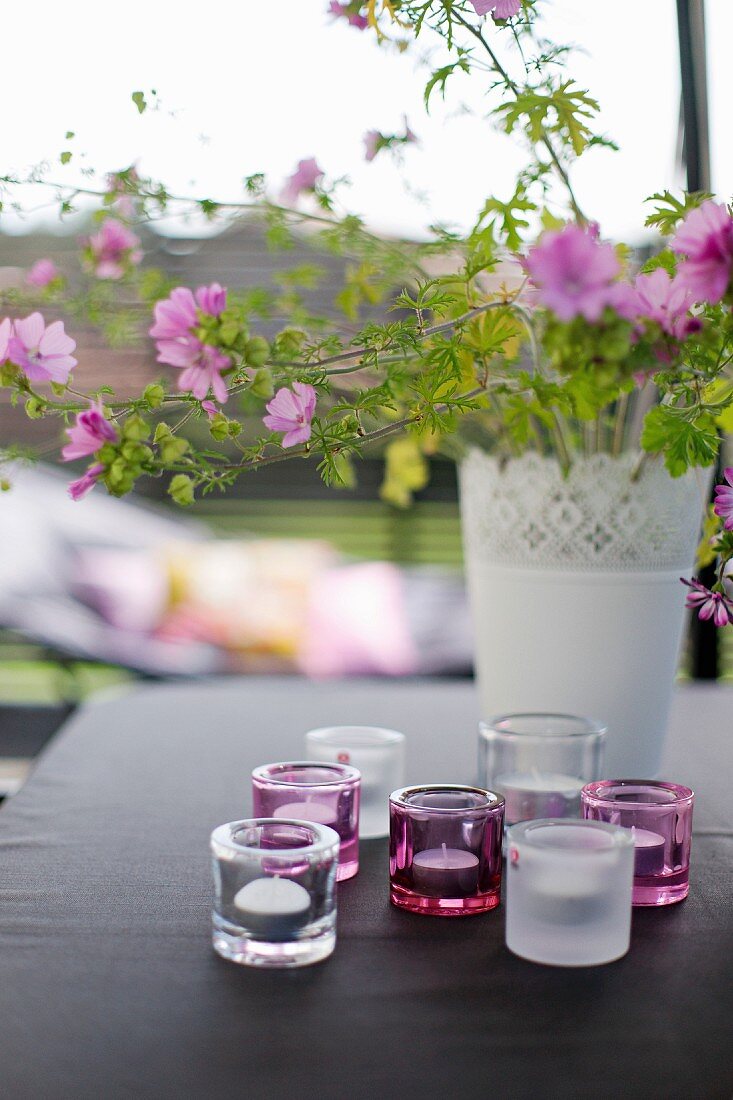 Lila Gartenstrauss in weisser Vase und Windlichter auf Tisch mit schwarzem Tischtuch