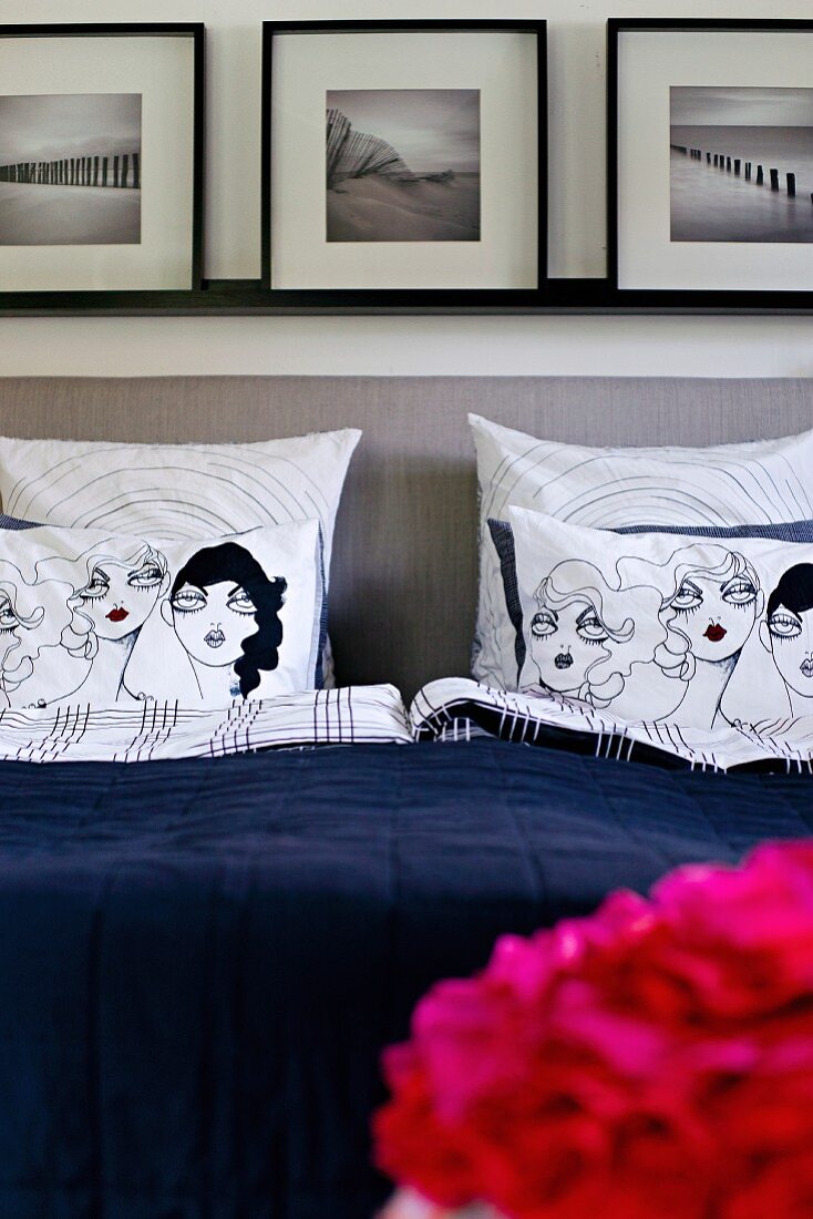 Comicartige Zeichnung auf Kissen im Bett, gepolstertes Kopfteil vor Wand mit gerahmter Bildersammlung