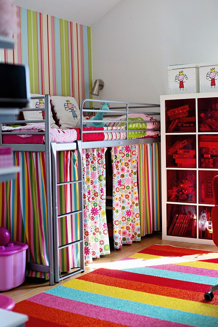 Metall Stockbett mit bunten Vorhängen in Kinderzimmerecke, davor Streifen Teppich