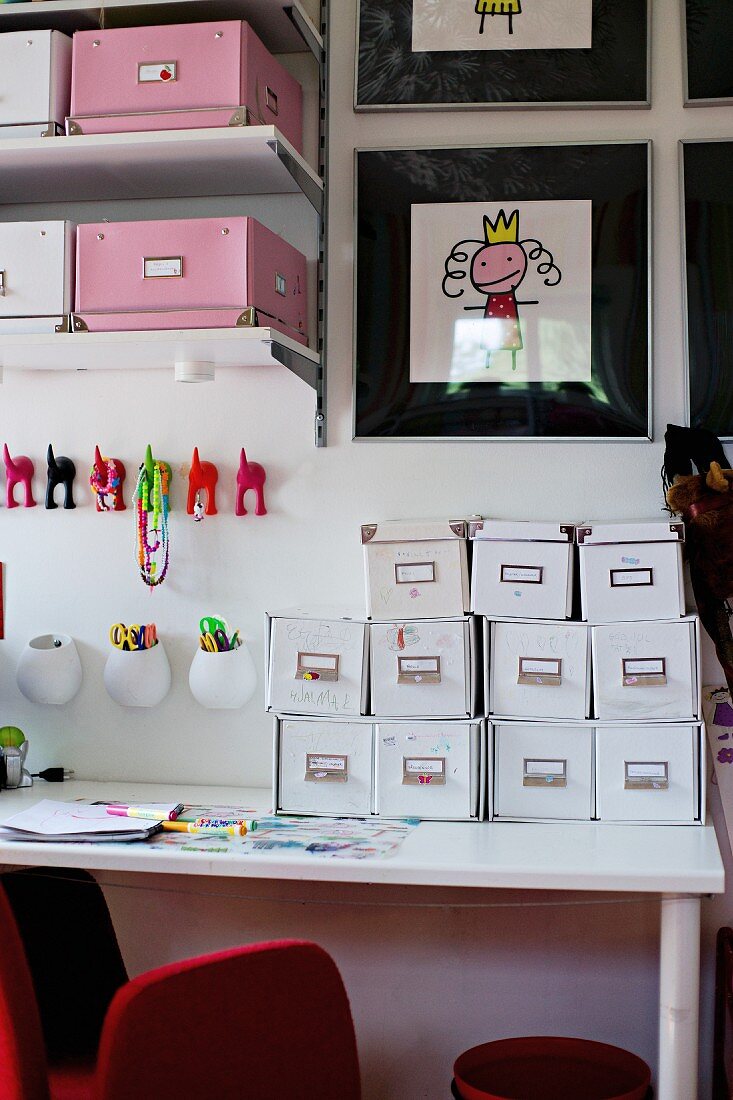 weiße Karteikästen auf Schreibtisch, vor Wand mit bunten Haken und Regalen mit rosa und weissen Ordnungsboxen