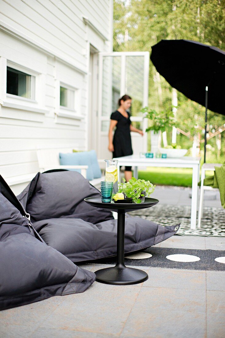 Schwarze Sitzsäcke um Beistelltisch, im Hintergrund Tisch unter schwarzen Schirm, Frau vor Terrassentür