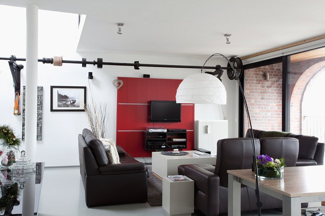 Lounge area with black leather sofa set opposite flatscreen TV and shelves on red wall-mounted panels in loft-style apartment