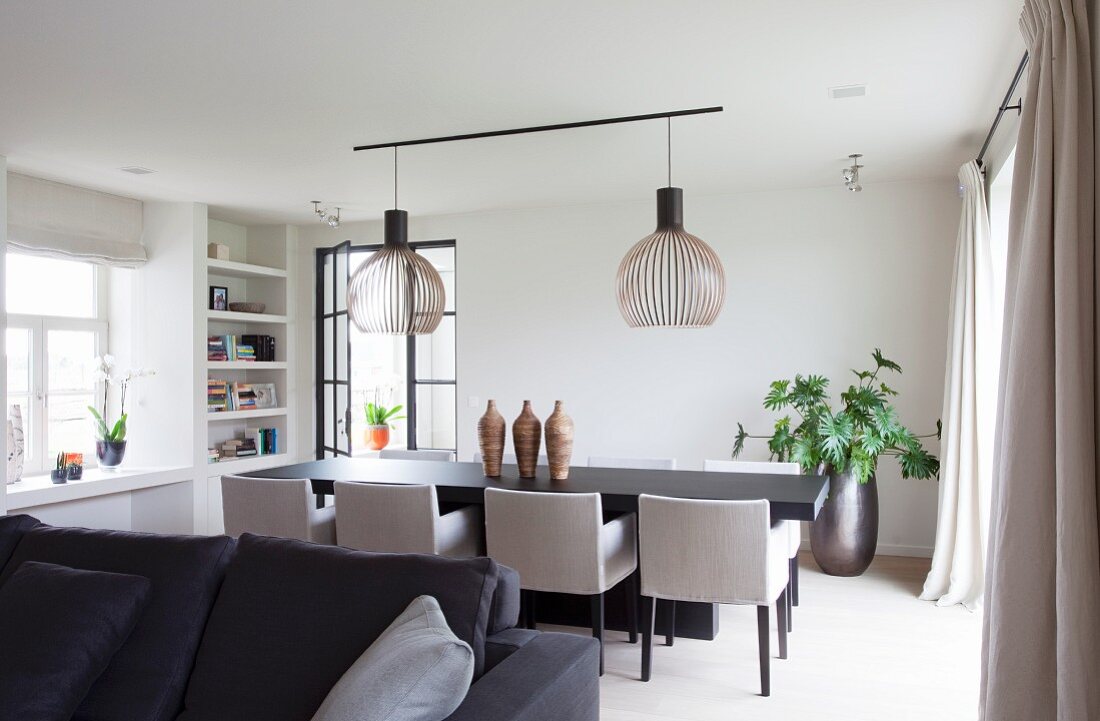 Elegant dining area, upholstered chairs around dark table below designer pendant lamps with wooden slatted lampshades