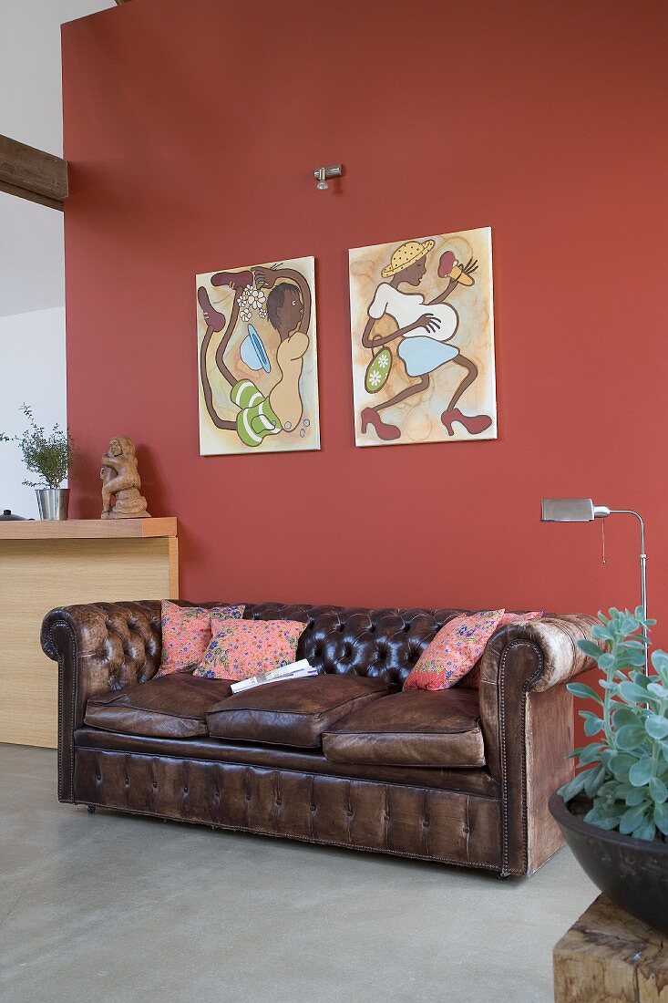 Braune Vintage Ledercouch an rotbrauner Wand mit Bildern in modernem Ambiente