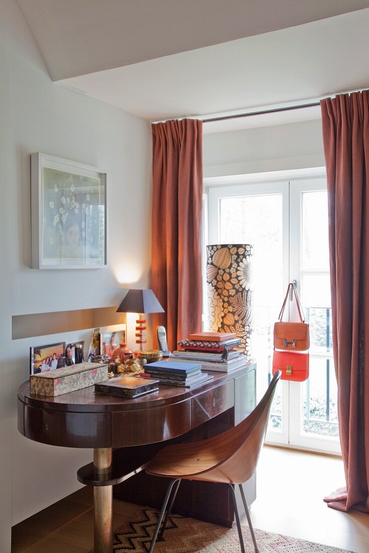 Abgerundeter Schreibtisch und Holzschalen Stuhl im Retro-Look vor Fenstertür mit bodenlangem Vorhang