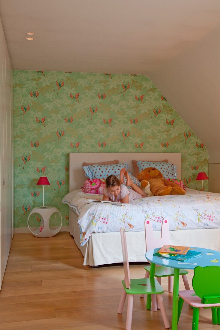 Child's attic bedroom, girl on double bed, table and small chairs in foreground painted pink and green