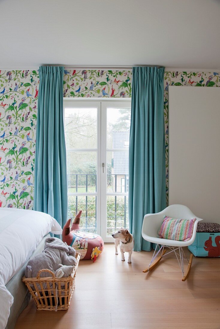 Kinderzimmer mit Klassiker Schaukelstuhl vor Fenstertür mit hellblauen, bodenlangen Vorhängen