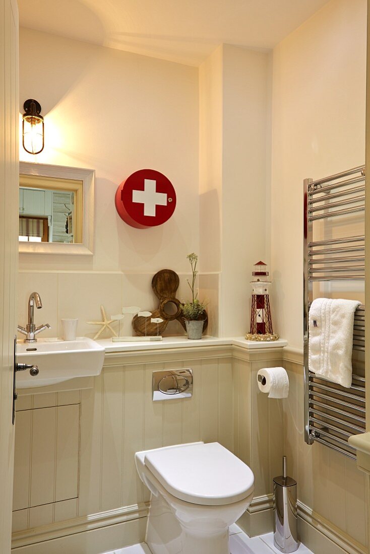 Blick ins Bad auf Toilette und Waschtisch vor halbhoher Holzverkleidung, an Wand Erste-Hilfe-Schränkchen
