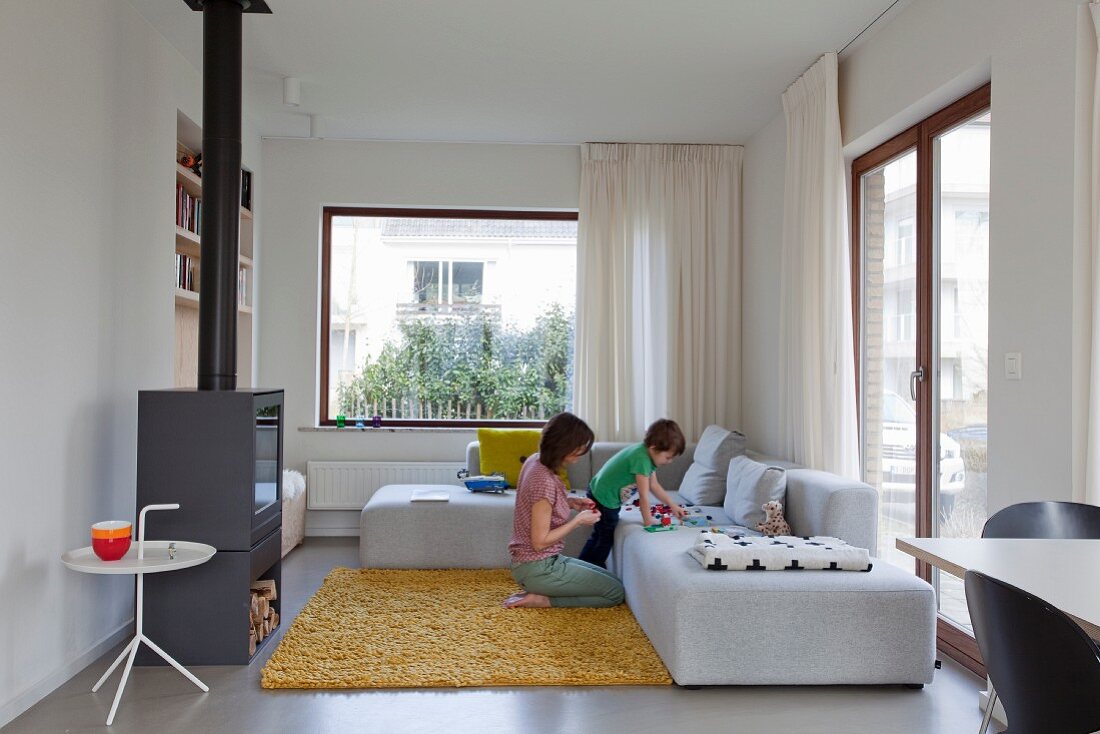 Pale grey corner sofa in modern lounge area; mother and child playing on yellow long-pile rug