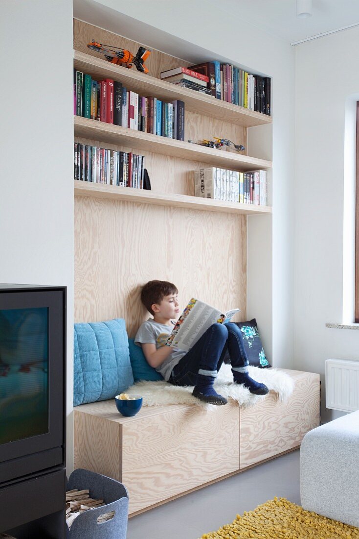 Boy reading on bench built into wood-panelled niche below bookshelves