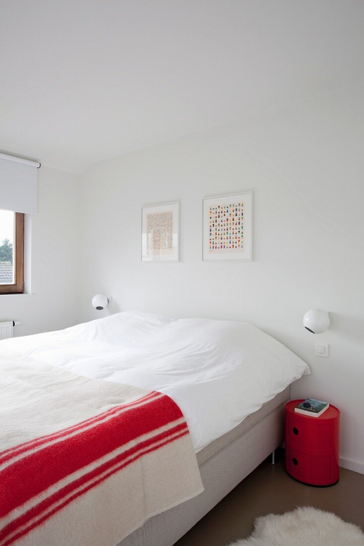 Elternschlafzimmer mit kugelförmigen Wandleuchten neben Doppelbett, darauf rotweiss gestreiftes Plaid, seitlich zylindrisches Nachtschränkchen in Rot