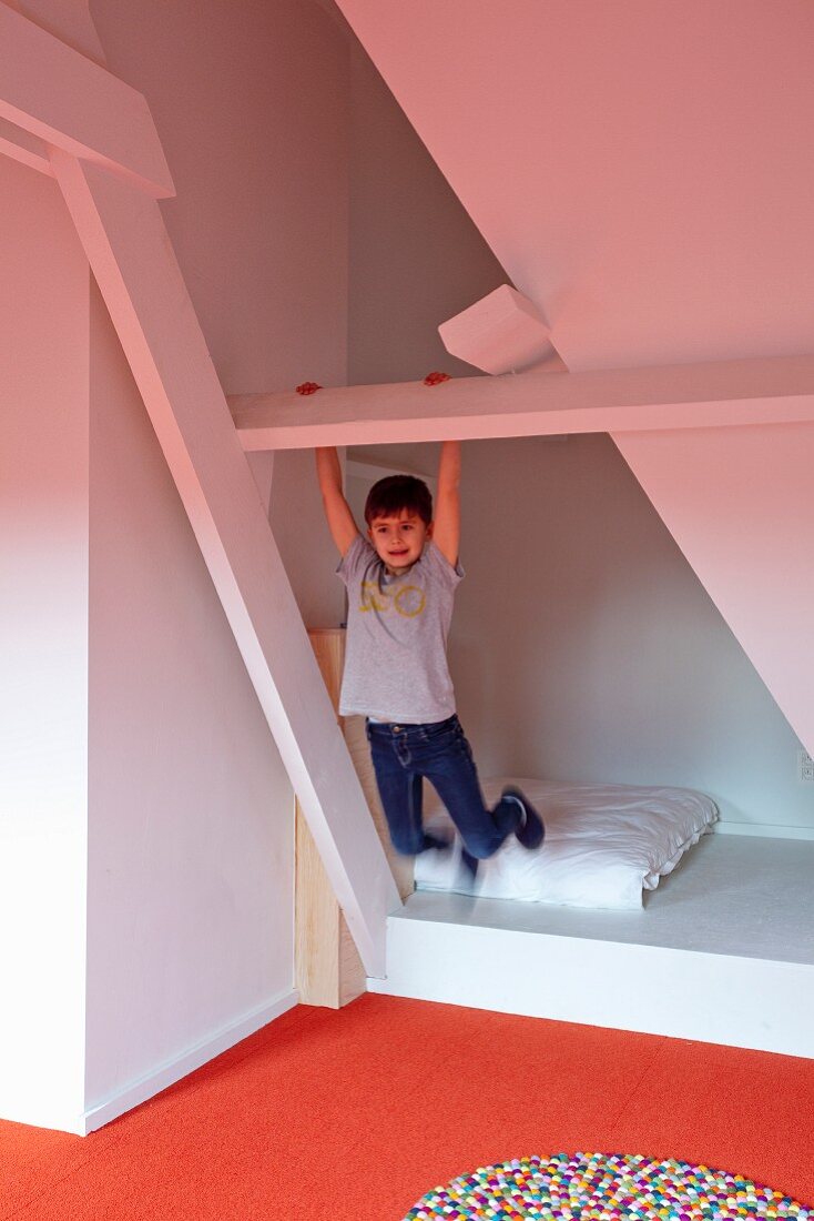 Junge in ausgebautem Dachzimmer beim Turnen an weißer Holzkonstruktion