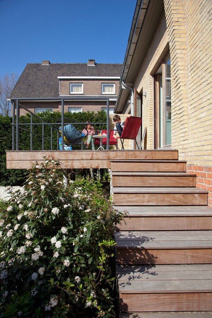 Summer day - steps leading to wooden terrace with family sitting on garden chairs