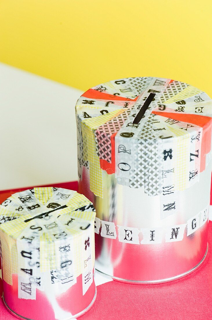 Empty paint tins decorated with washi tape and with slots in top used as money boxes