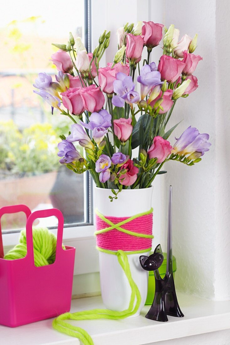 Blumenstrauss aus lila Freesien und Eustoma in Blumenvase, mit bunten Wollgarnen umwickelt