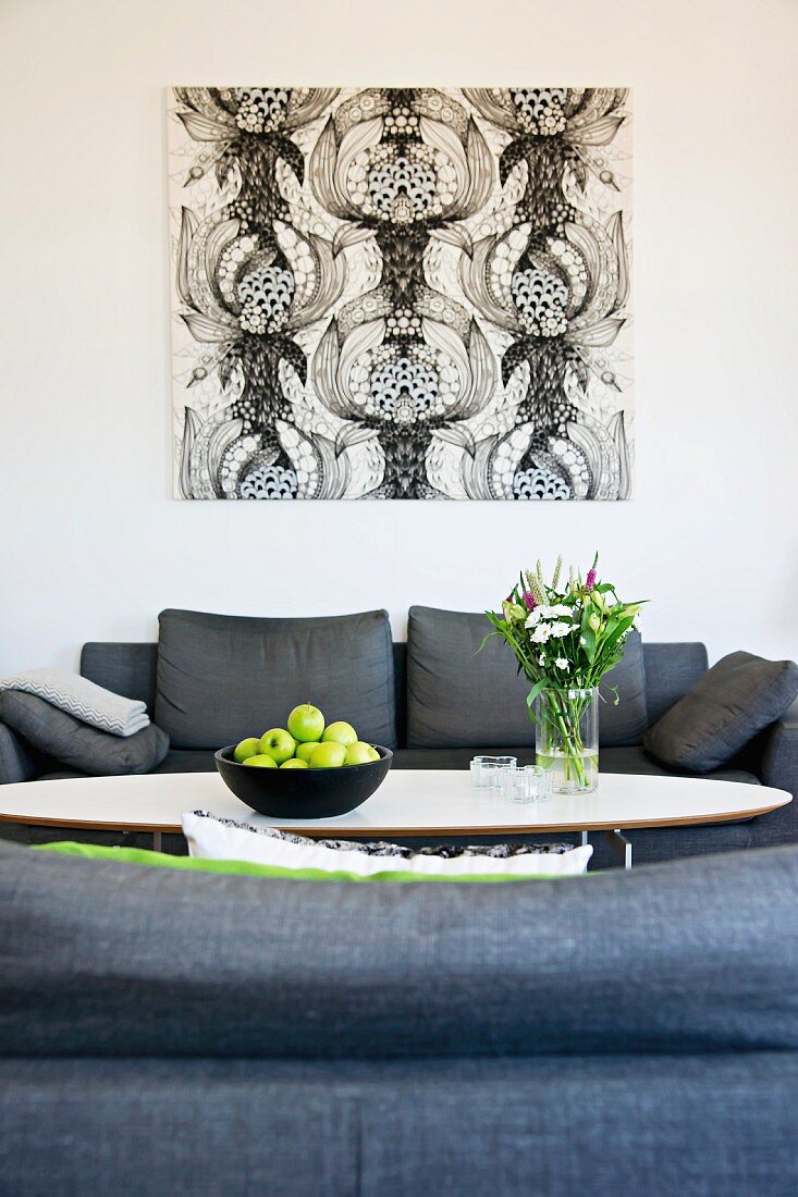 Blick über graue Sofagarnitur und Obstschale auf Klassiker Coffee Table, an Wand Bild mit schwarzweissem, grafischem Muster